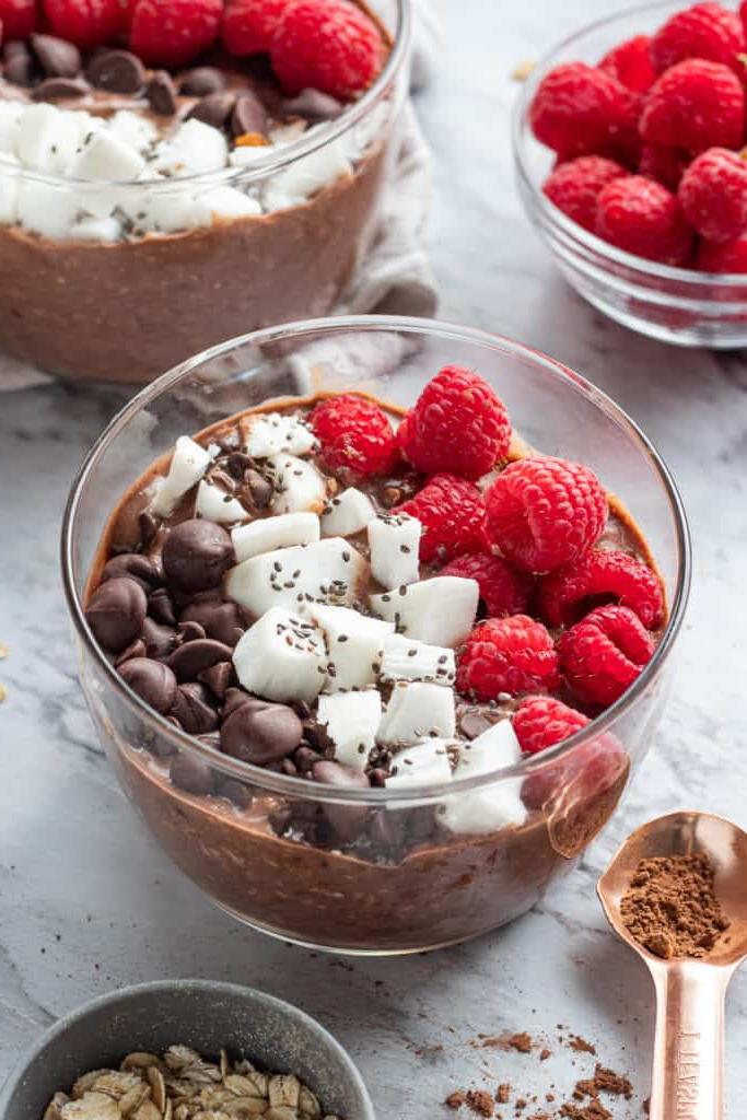 Glass bowl of chocolate overnight oats with coconut and raspberries.