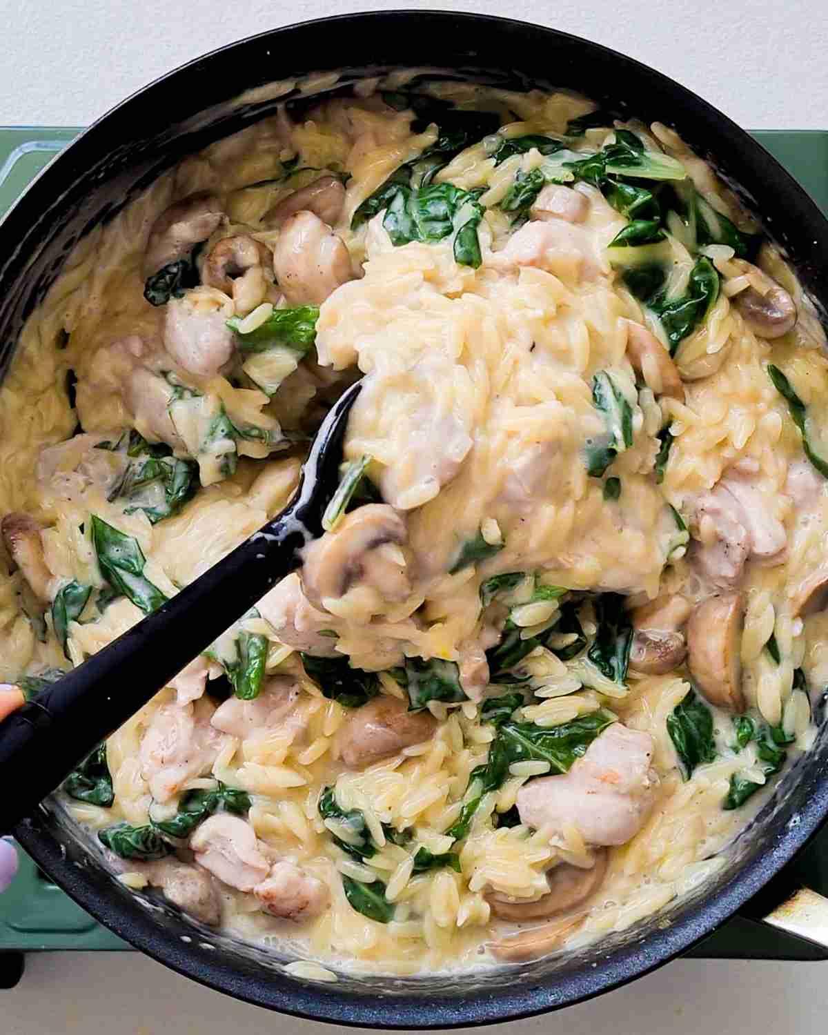 Creamy chicken orzo being stirred in a large cooking saute pan