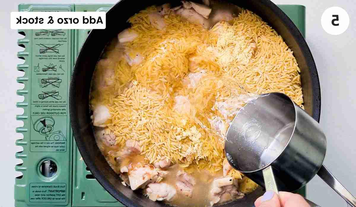 water being poured in a pan filled with uncooked orzo and chicken cubes