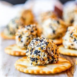 Cheese Ball Bite on a round cracker on a marble and wood cutting board.
