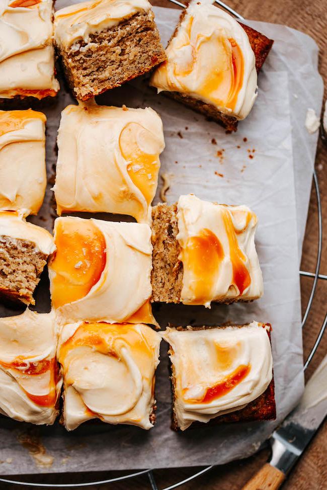 salted caramel frosted banana snack cake sliced on parchment covered cooling rack