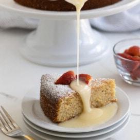 A golden slice of lemon olive oil cake, made wit whole almonds, served with berries and glaze.