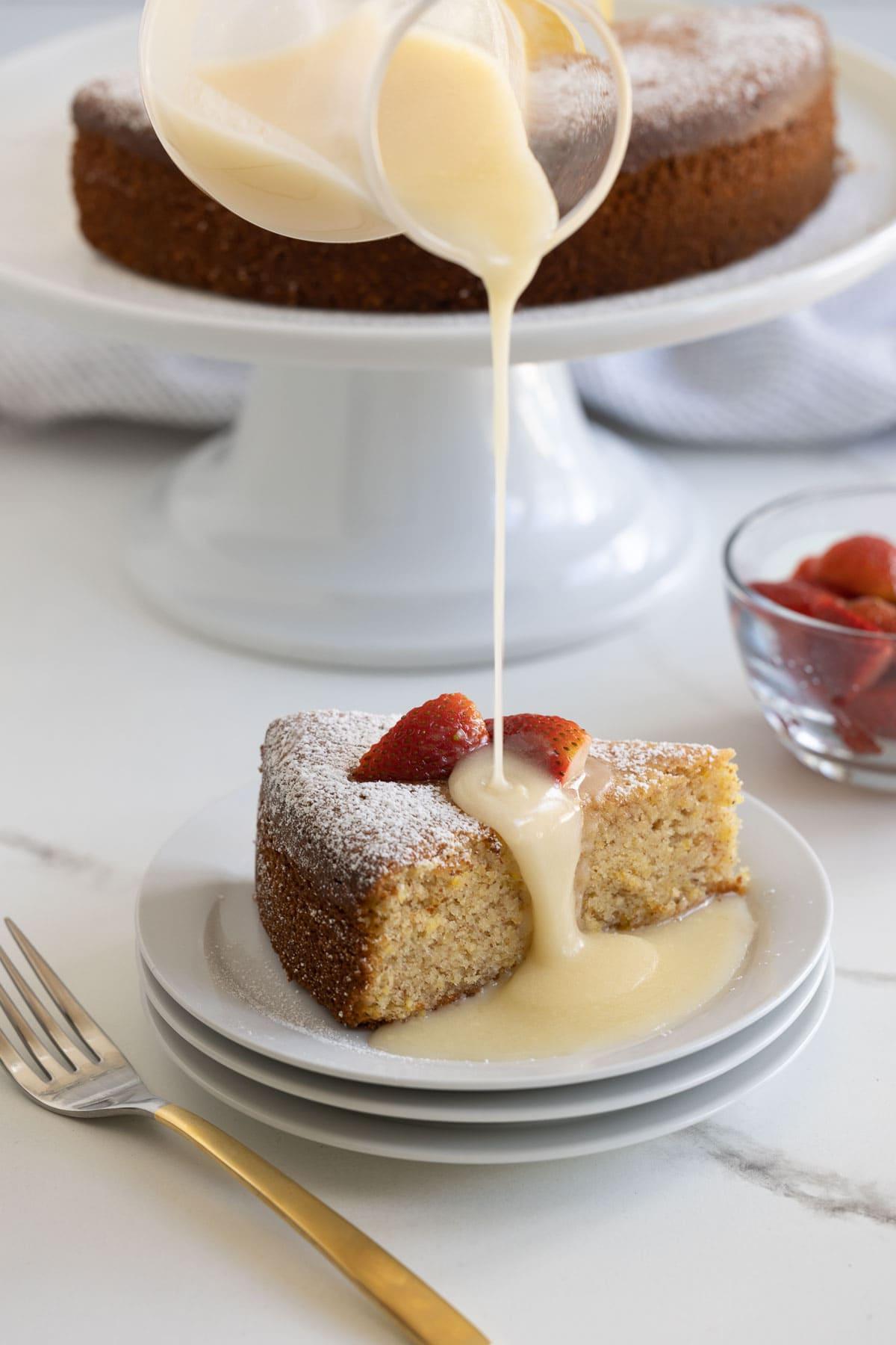 A slice of lemon olive oil cake drizzled with lemon glaze, the cake behind.