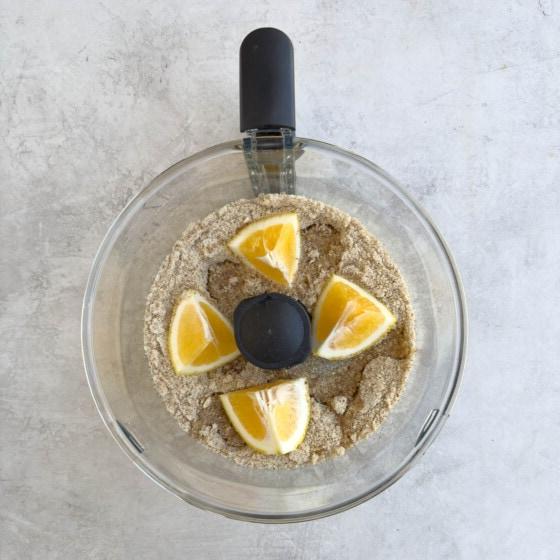 Grinding whole almonds, sugar, and lemon in a food processor bowl.