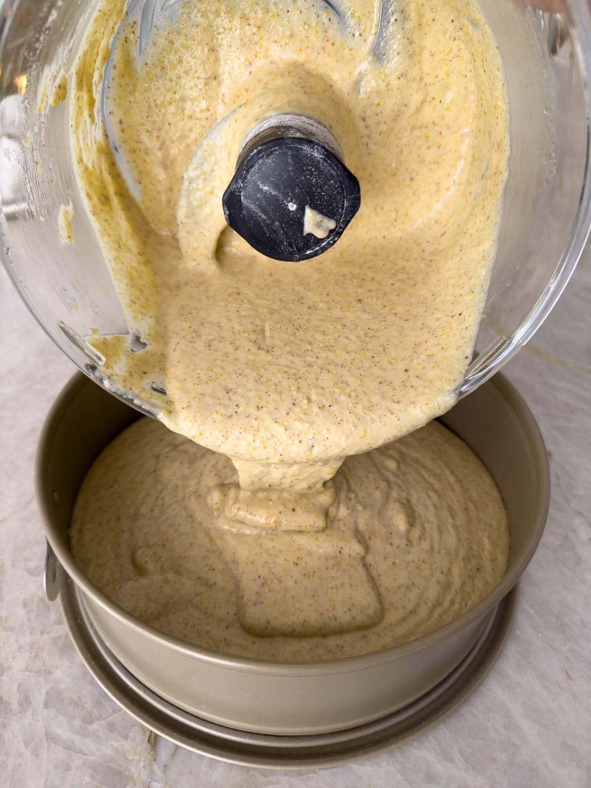 Pouring olive oil almond cake batter from the workbowl into the springform pan for baking.